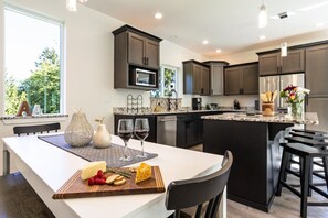 A modern kitchen with dark cabinetry, a central island, and a dining area with a white table.