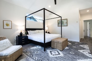 A four-poster canopy bed with a white bedspread, a nightstand with a lamp, a wicker chair, and a patterned rug. - Luxury 4BR in the Foothills · Lake & Trails · Sleeps 8 (Sedro-Woolley)