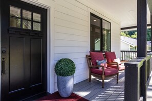 A porch with a door, a potted plant, and two chairs with cushions.