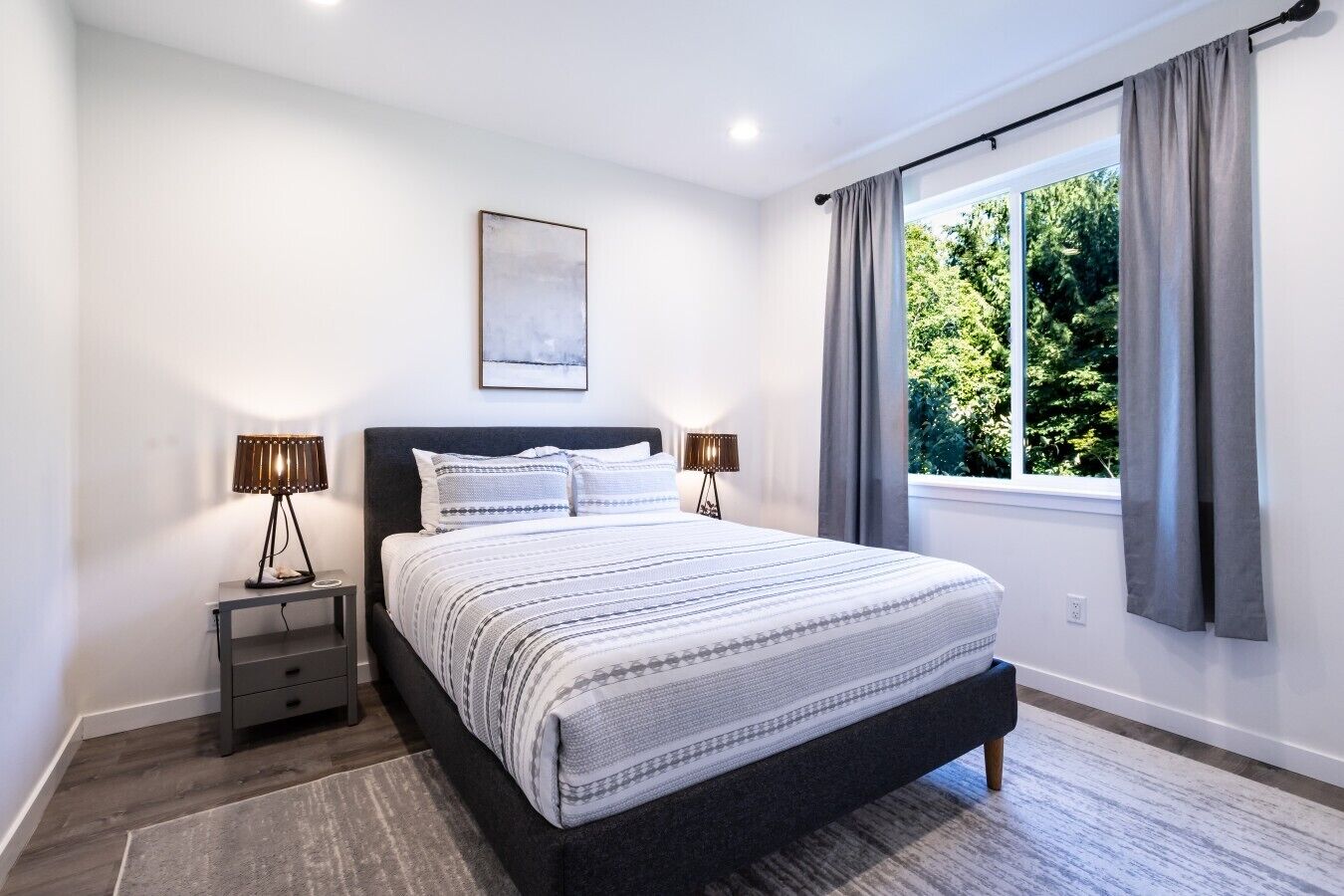 Een moderne slaapkamer met een groot bed, nachtlampjes, een raam met gordijnen en een ingelijst schilderij aan de muur.