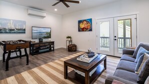 A living room with a foosball table, a television, a ceiling fan, and a large window with a view. - Luxury 4BR in the Foothills · Lake & Trails · Sleeps 8 (Sedro-Woolley)