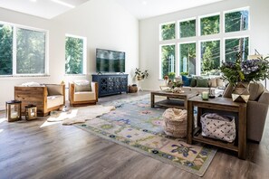 A spacious living room with a large window, a television, a sofa, a coffee table, and a rug.