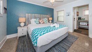 A bedroom with a bed, nightstands, a ceiling fan, and a view into the kitchen area.
