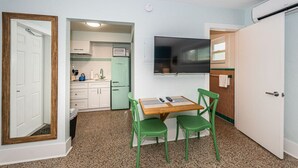 Cocina compacta con microondas, lavaplatos y armarios, una pequeña mesa de comedor con sillas y un televisor montado en la pared.