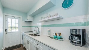 A kitchen with white cabinets, a stainless steel sink, a coffee maker, and a clock on the wall.