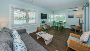 A living room with a sofa, coffee table, and chairs, a dining area with a table and chairs, and a TV mounted on the wall.