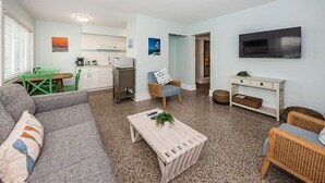 Ein kompakter Wohnbereich mit Küchenzeile, einem Essbereich, einer Sitzecke inklusive Sofa und Sesseln sowie einem an der Wand befestigten Fernseher.