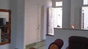 Ein geräumiges Wohnzimmer mit einem großen Spiegel, zwei Holzstühlen, einer Kronleuchter und Blick durch ein Fenster ins Freie.
