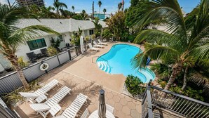 A pool area with lounge chairs, a small table, and a surfboard.