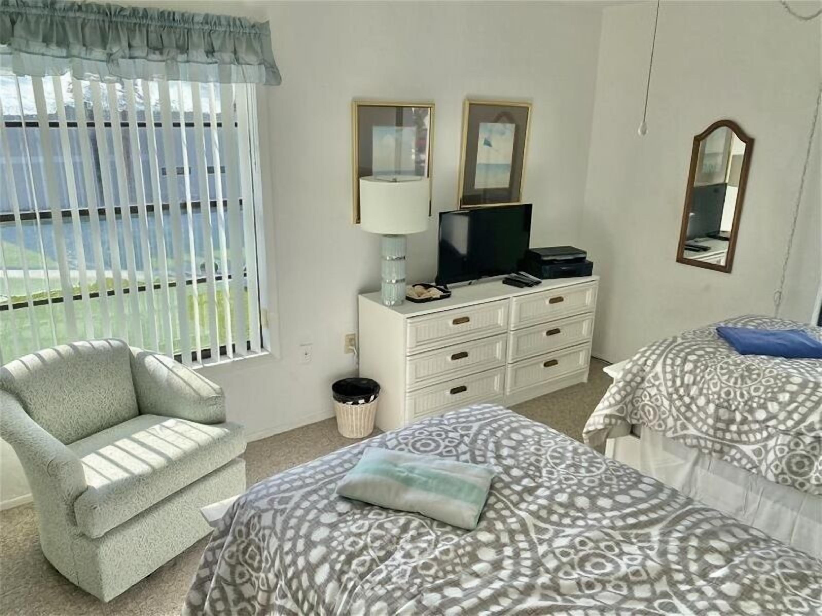 A room with a sofa, a bed with patterned bedding, a TV on a dresser, and a window with curtains.