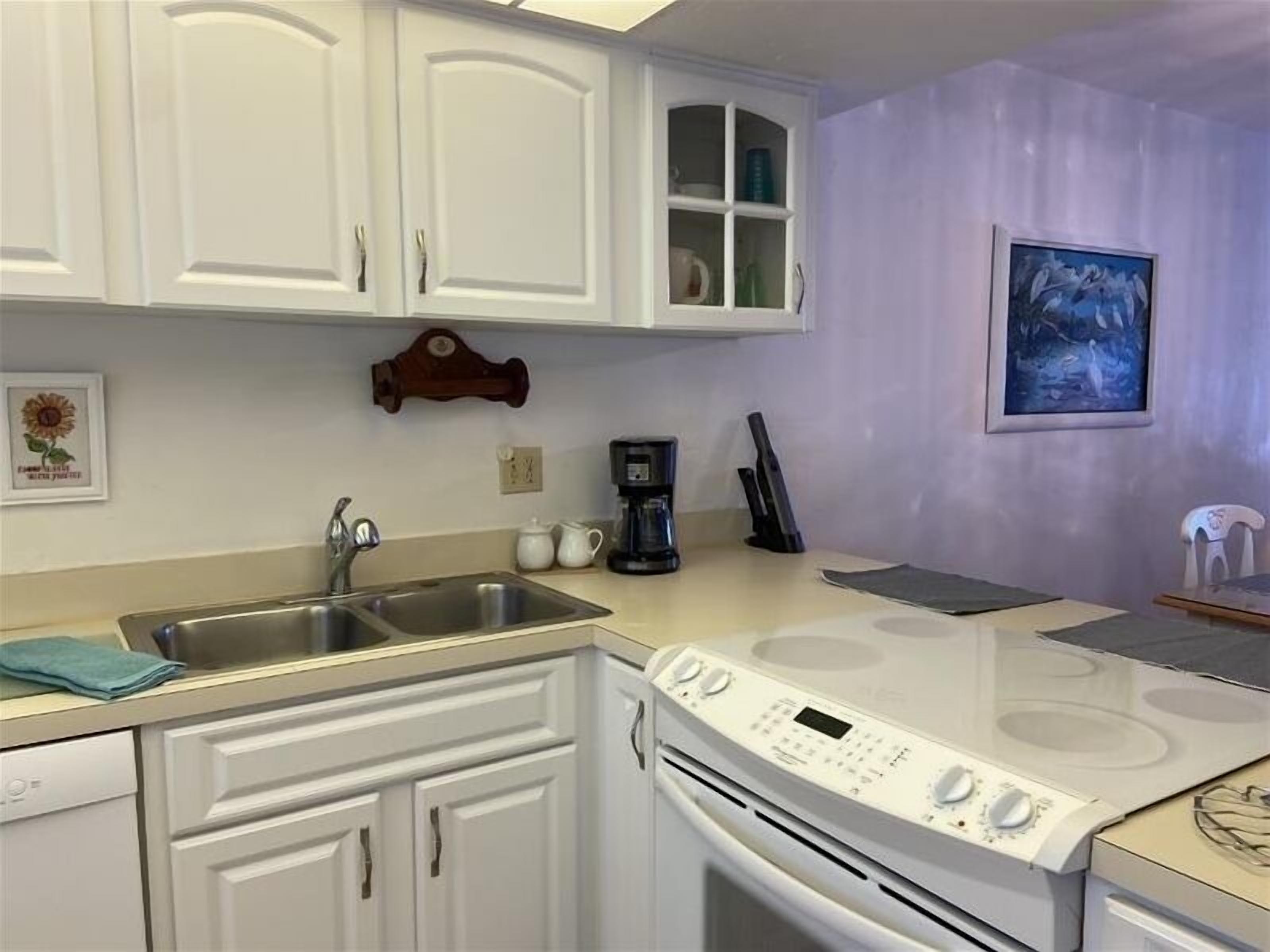A kitchen with white cabinets, a stainless steel sink, a coffee maker, and a stove.