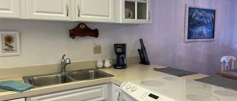 A kitchen with white cabinets, a stainless steel sink, a coffee maker, and a stove.