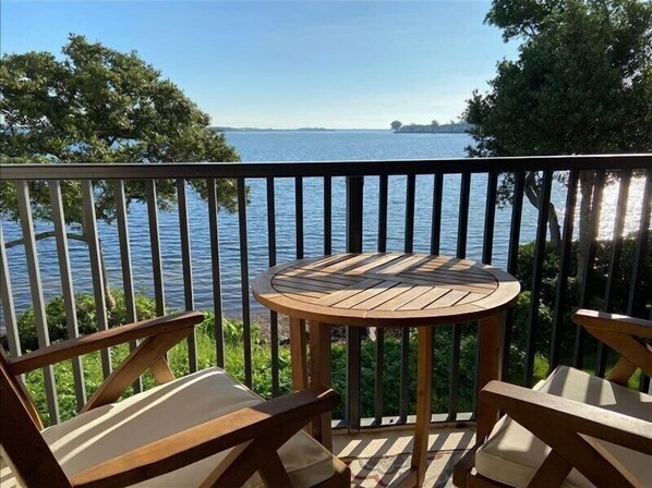 A wooden deck with a round table and two chairs, overlooking a body of water.