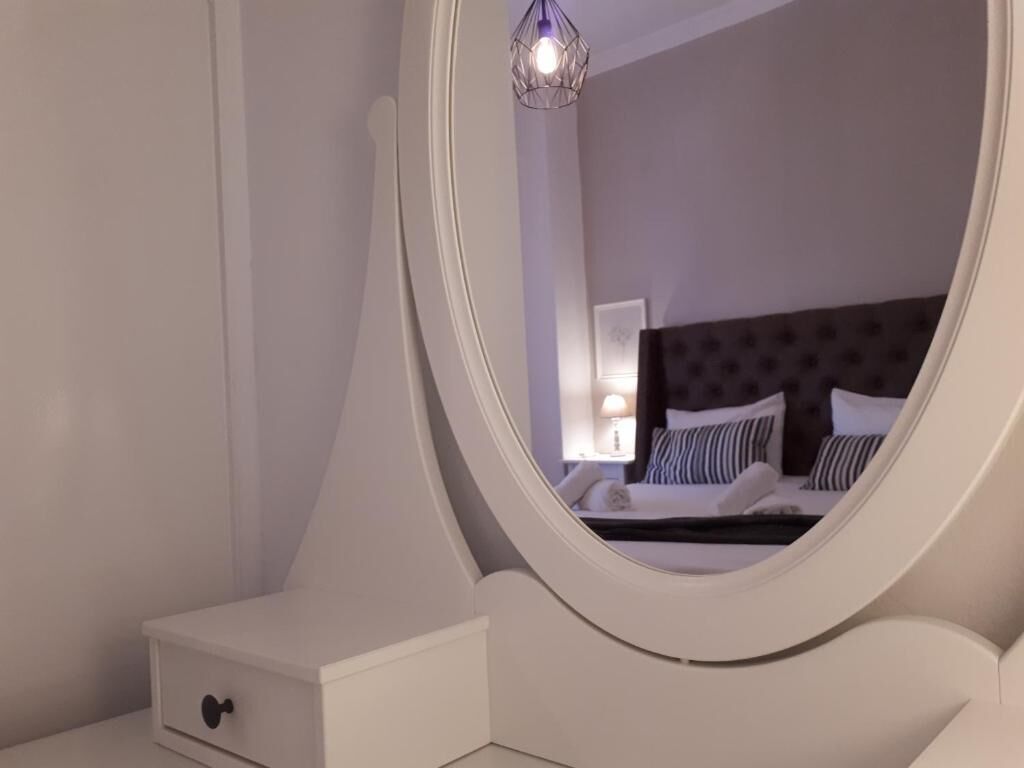 A bedroom with a white vanity, a round mirror, and a bed with striped pillows.
