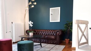 Een woonkamer met een donkere blauwe muur, een bruine leren bank, een ronde tafel, een witte stoel en een tapijtend met een patroon.