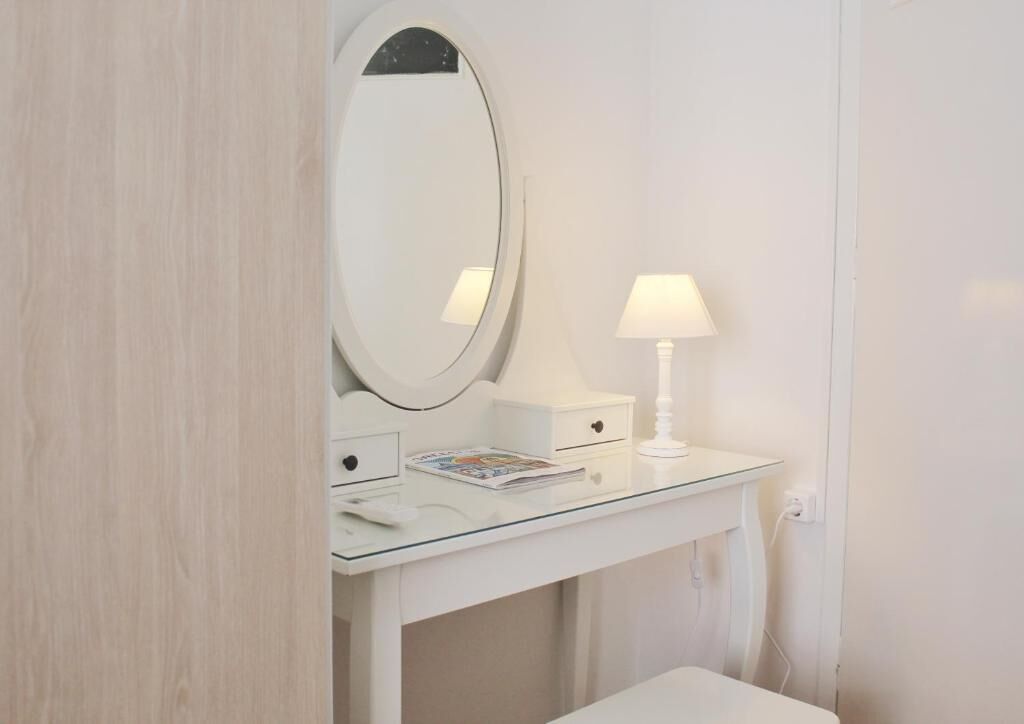 Une coiffeuse blanche avec un miroir rond, une petite table de chevet et une lampe.