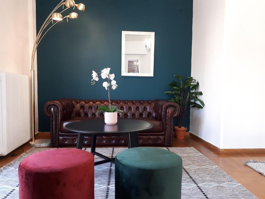 Une pièce avec un mur d’accent bleu foncé, un canapé en cuir marron, une table ronde agrémentée d’une plante en pot et deux poufs.