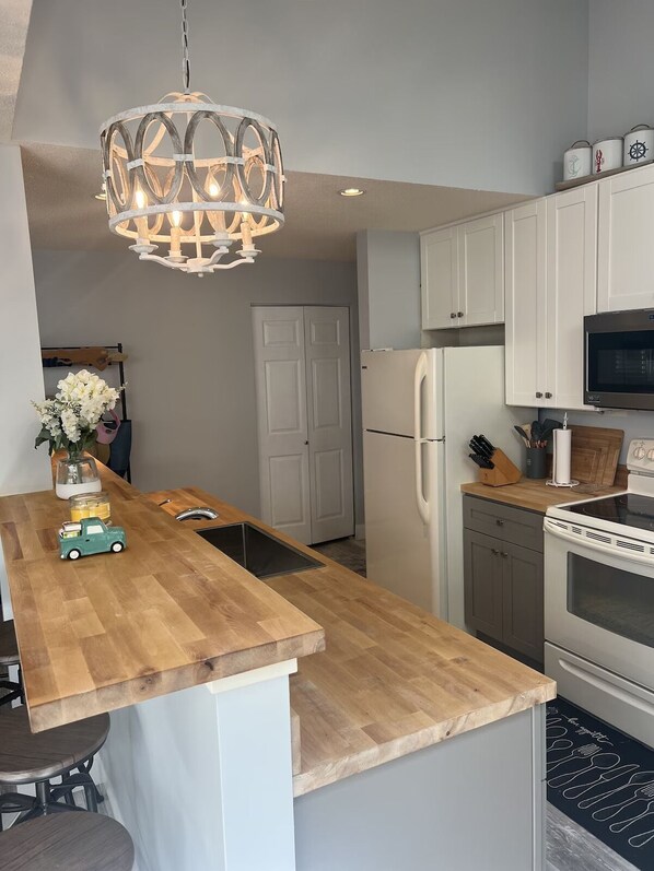 Una cocina moderna con una isla de madera, armarios blancos, un refrigerador de acero inoxidable y un horno empotrado.