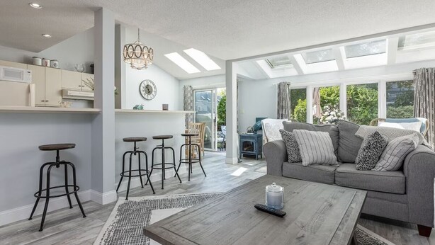 A spacious living area with a grey sofa, wooden coffee table, and black bar stools.