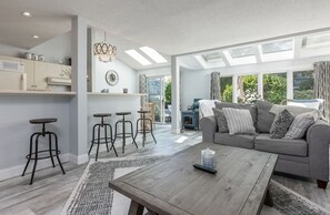 Amplia sala de estar con sofá gris, mesa de centro de madera y taburetes negros.