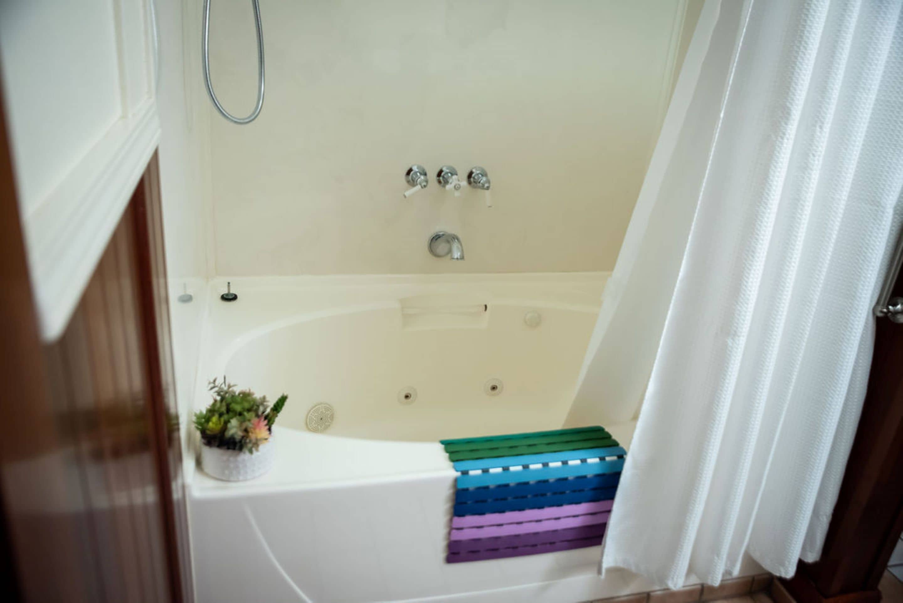 A bathtub with a showerhead, a small plant, and a towel rack with colorful towels.