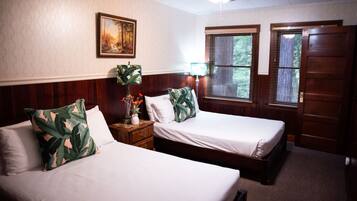A room with two beds, a ceiling fan, a painting on the wall, and a window with blinds.