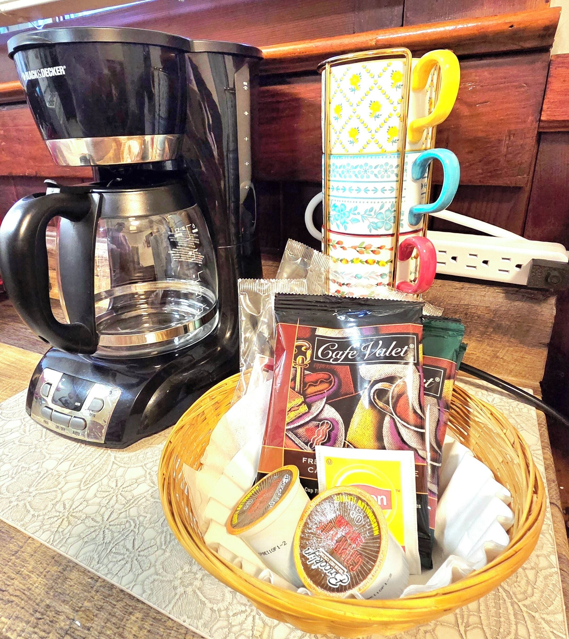 Une machine à café, une tasse et un panier contenant des dosettes de café et un sachet de thé, posés sur un plan de travail de cuisine.