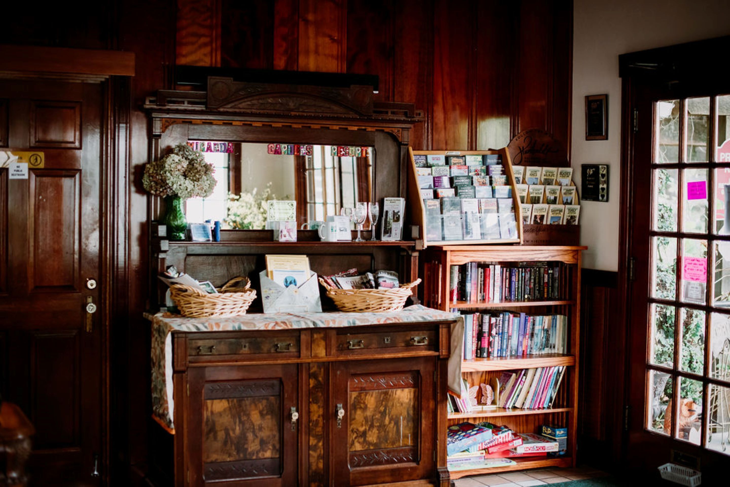 A wooden interior with a bookcase, a counter with baskets, and a window with a view.