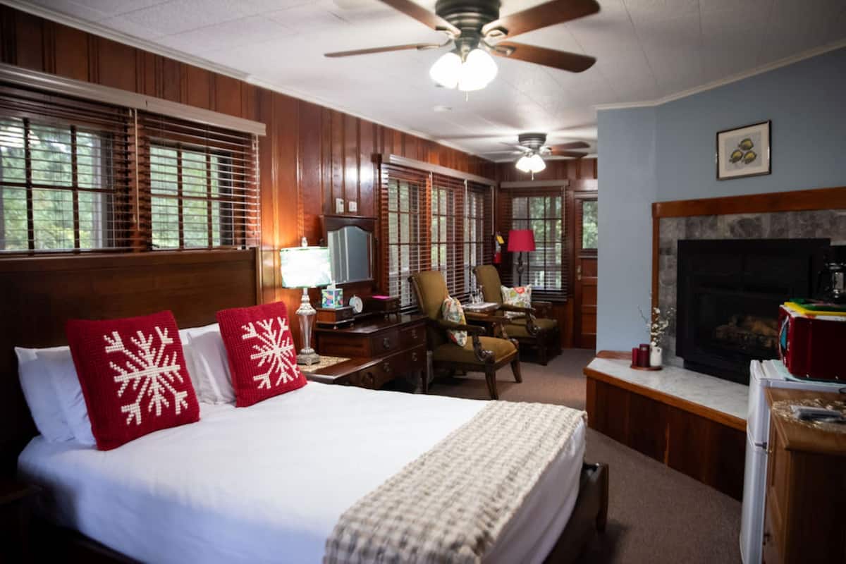 A hotel room with a large bed, wooden paneling, a fireplace, a desk with a lamp, and a chair.
