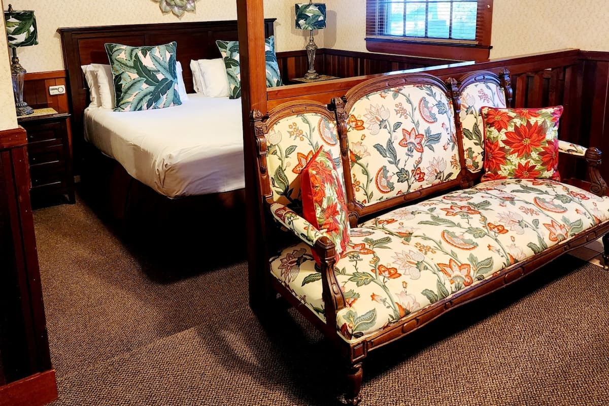 A bedroom with a four-poster bed, a floral sofa, and a window with blinds.