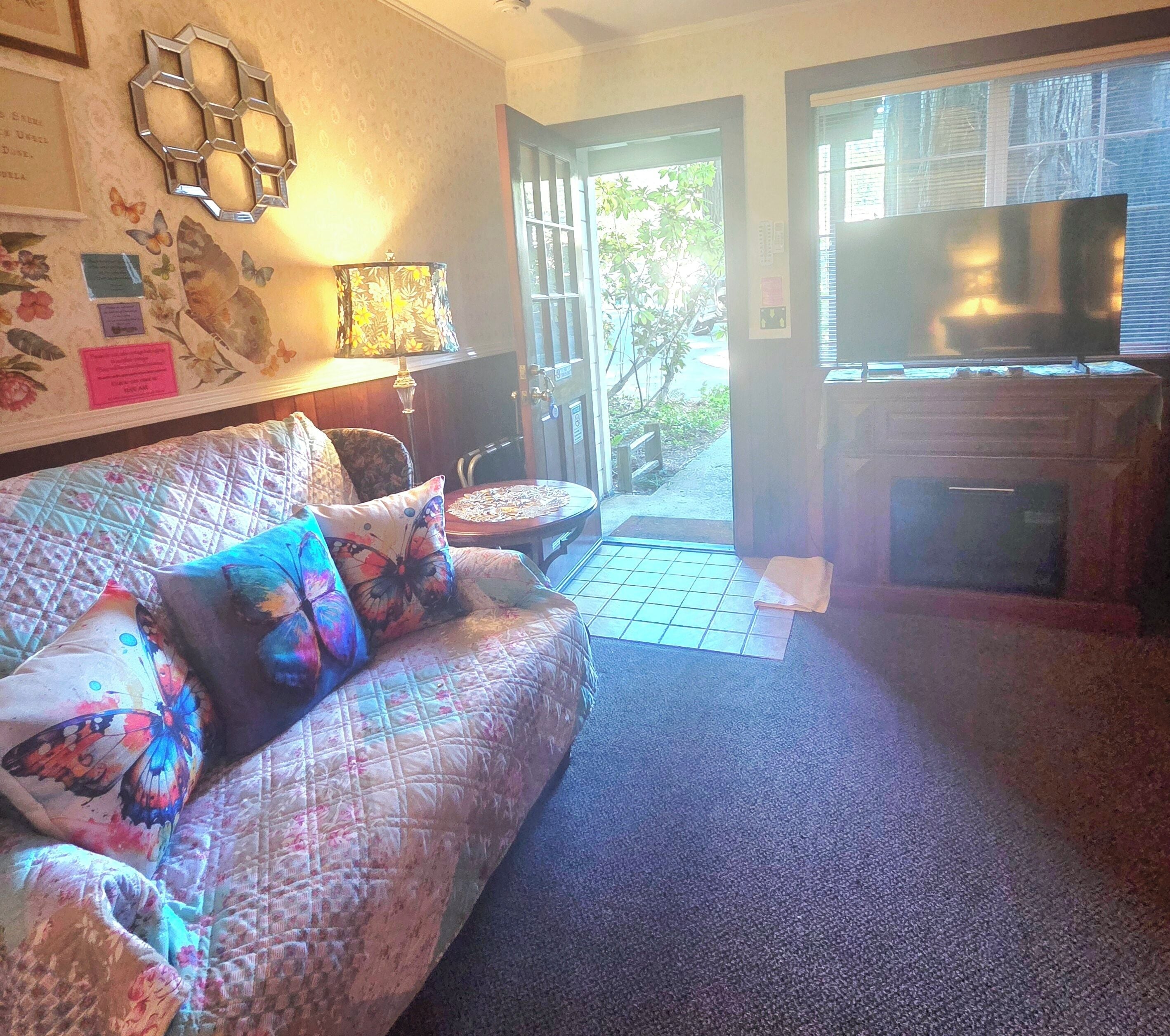 A living room with a sofa, a table, a lamp, a fireplace, and a door leading outside.