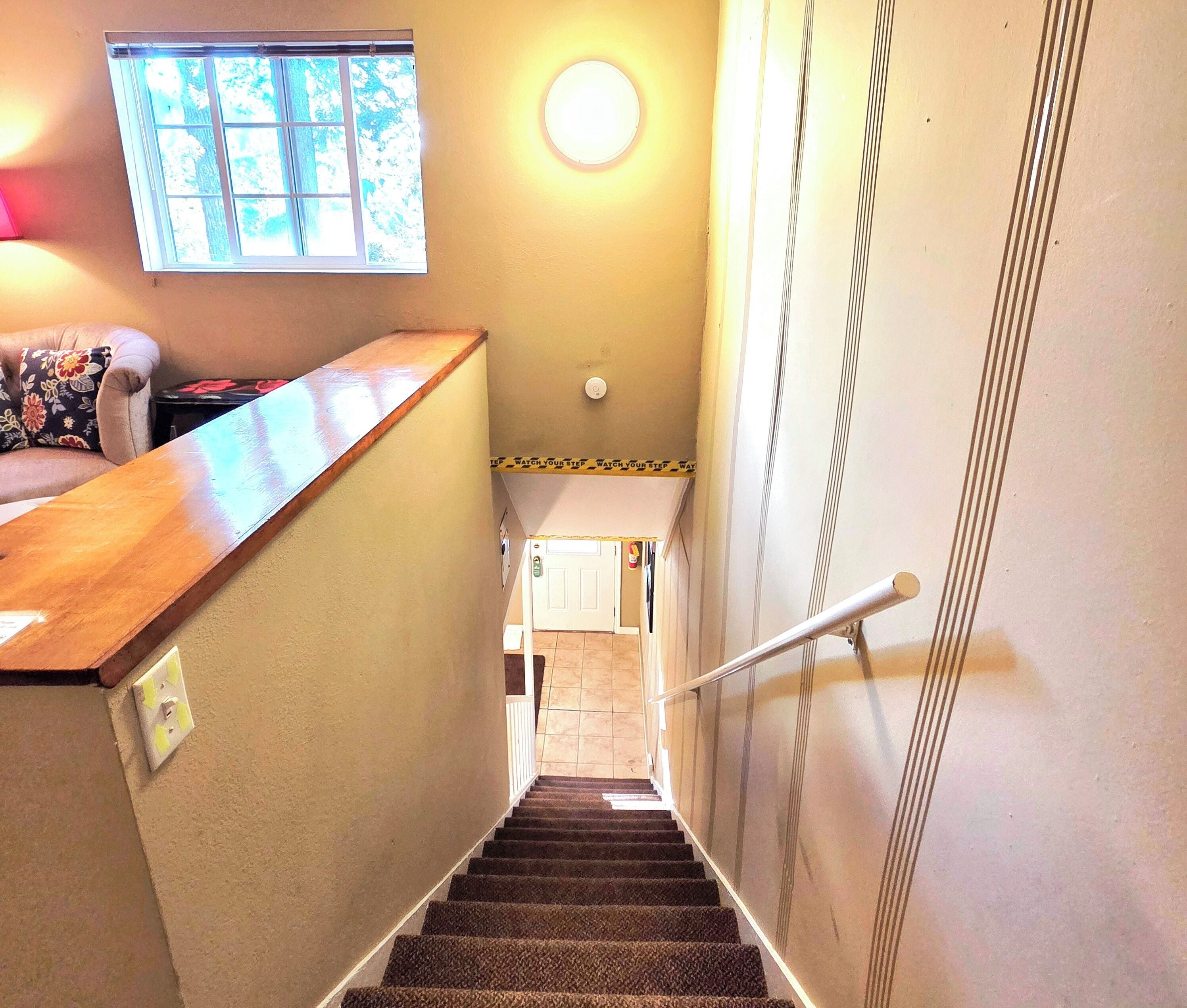 A staircase with carpeted steps, a handrail, a wooden counter, a window with a view of trees, and a door at the bottom.