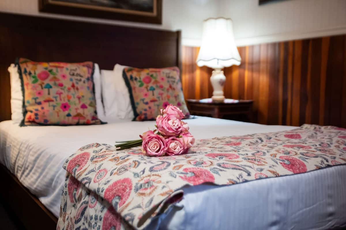 A neatly made bed with floral-patterned bedding and a bouquet of pink roses.