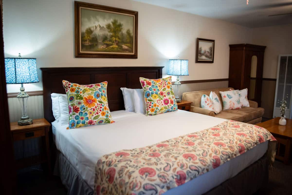 A hotel room with a large bed, two bedside tables, a nightstand, a wooden headboard, a sofa, and a painting on the wall.