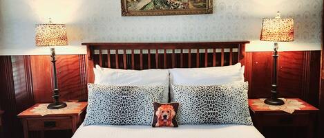 A neatly made bed with two pillows, a framed painting above, and two bedside lamps on wooden nightstands.