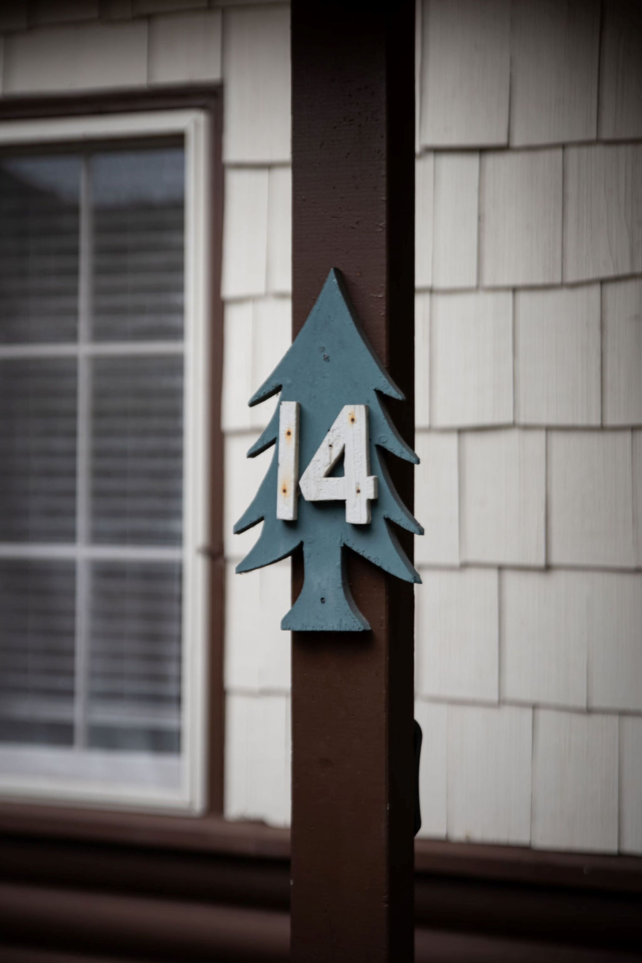 A house number '14' on a brown post with a tree design.