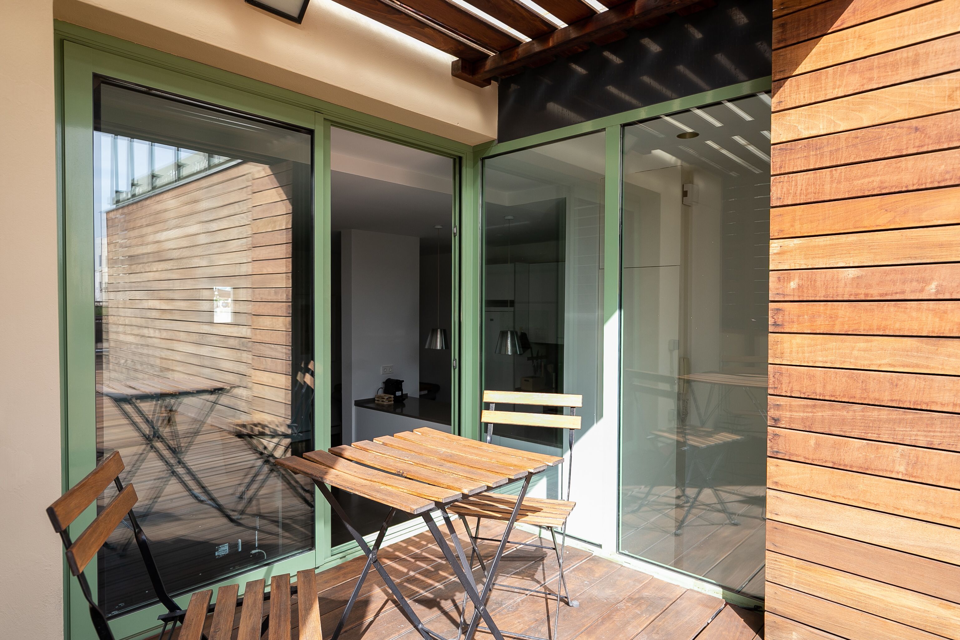 Un patio moderno con una mesa y sillas de madera, una bicicleta afuera y una puerta corrediza de vidrio que da a un espacio interior.
