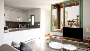 A modern kitchen with white cabinets, a black countertop, and a built-in microwave. There is a dining area with a table and chairs, and a large window with a view of the outside. - Apartment with spectacular terrace in the center of Barcelona (Barcelona)