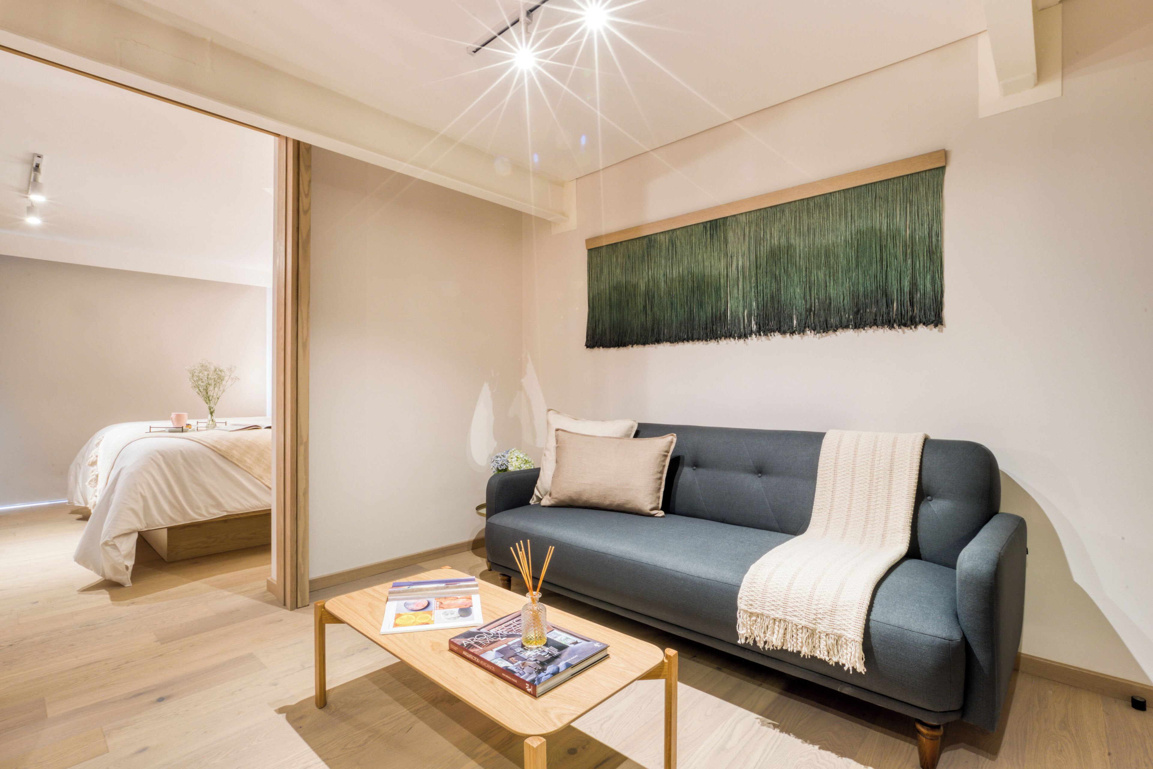 A modern living room with a grey sofa, a wooden coffee table, and a green textured wall hanging.