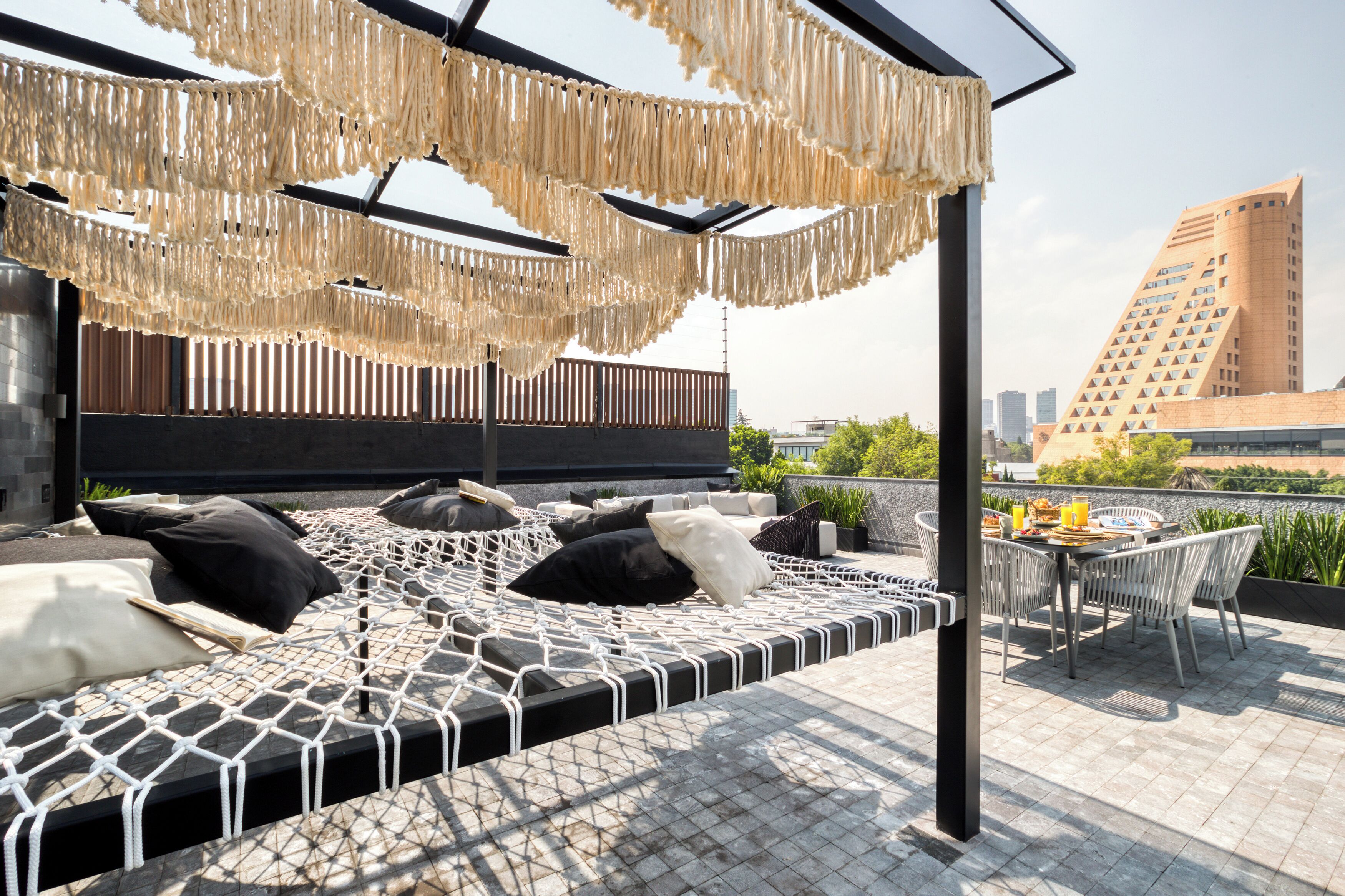 A rooftop lounge with a hammock bed, outdoor seating, and a view of the cityscape.