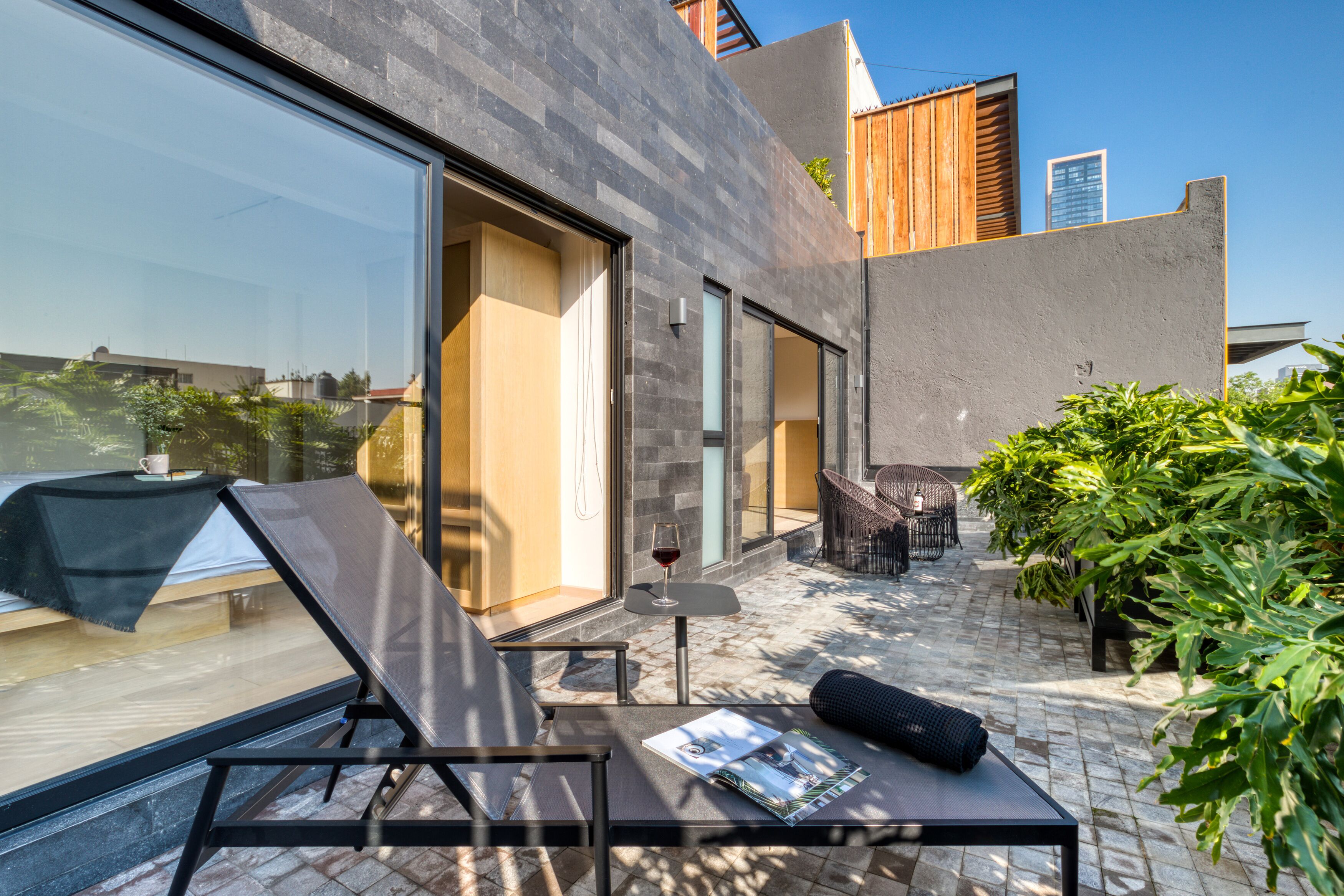 A modern outdoor seating area with a glass door, a table with a glass of red wine, and a magazine.