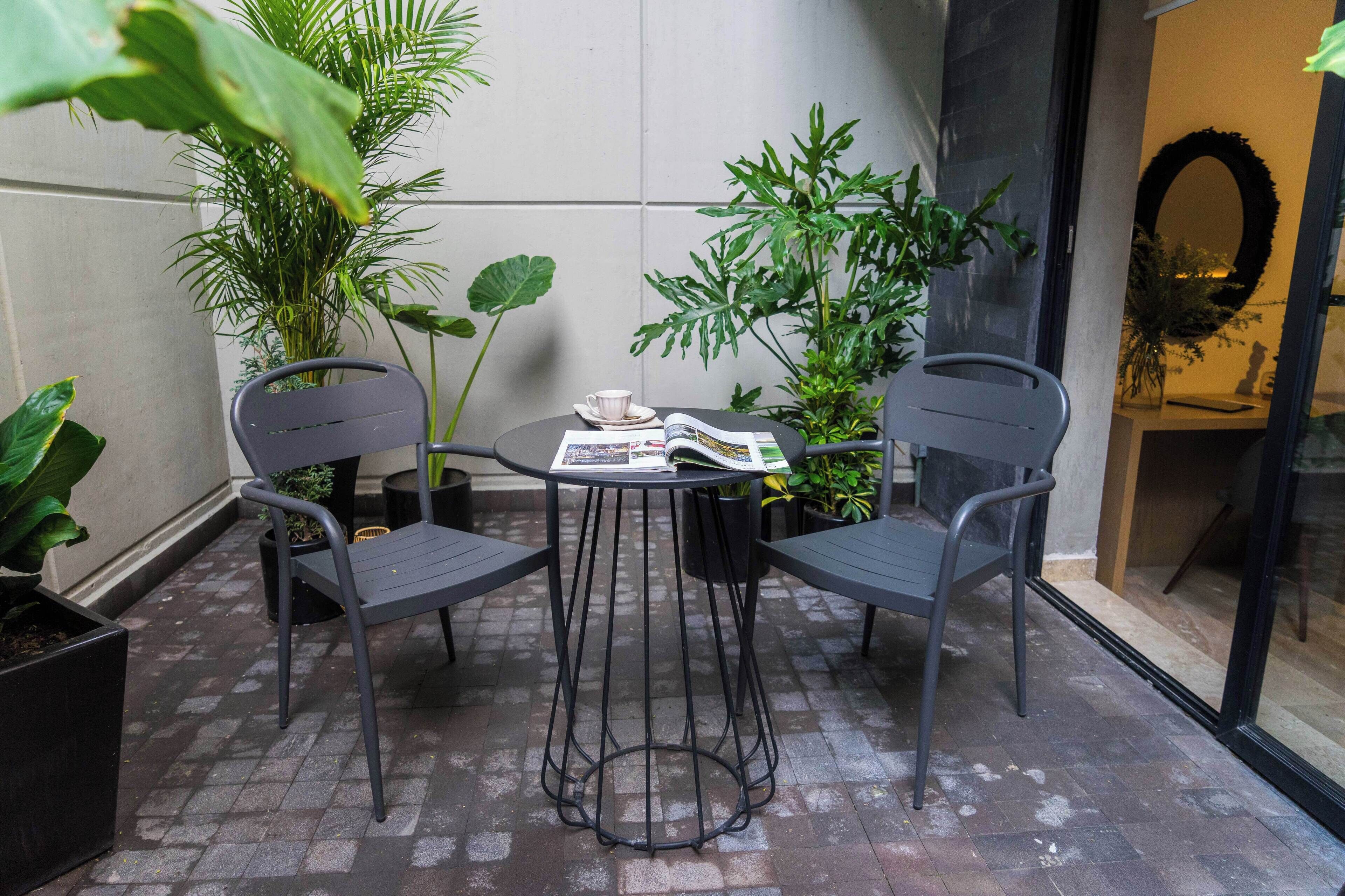 A small outdoor seating area with two chairs and a table, surrounded by potted plants.