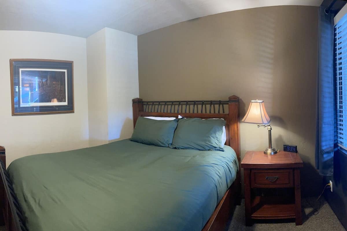 A bedroom with a bed, a bedside table with a lamp, a TV mounted on the wall, and a framed picture on the wall.