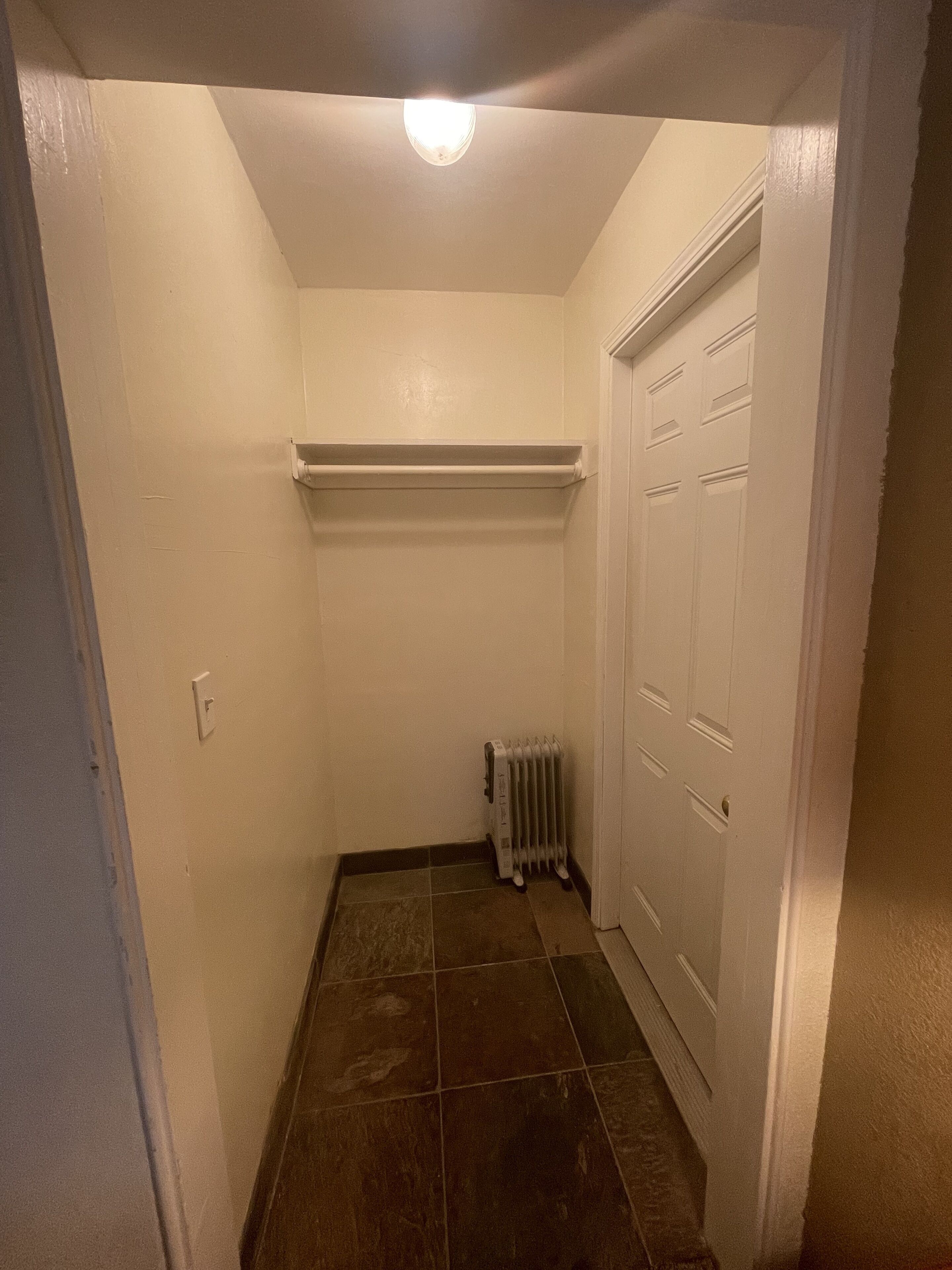Een smalle gang met een radiator, een witte deur en een lamp aan het plafond.