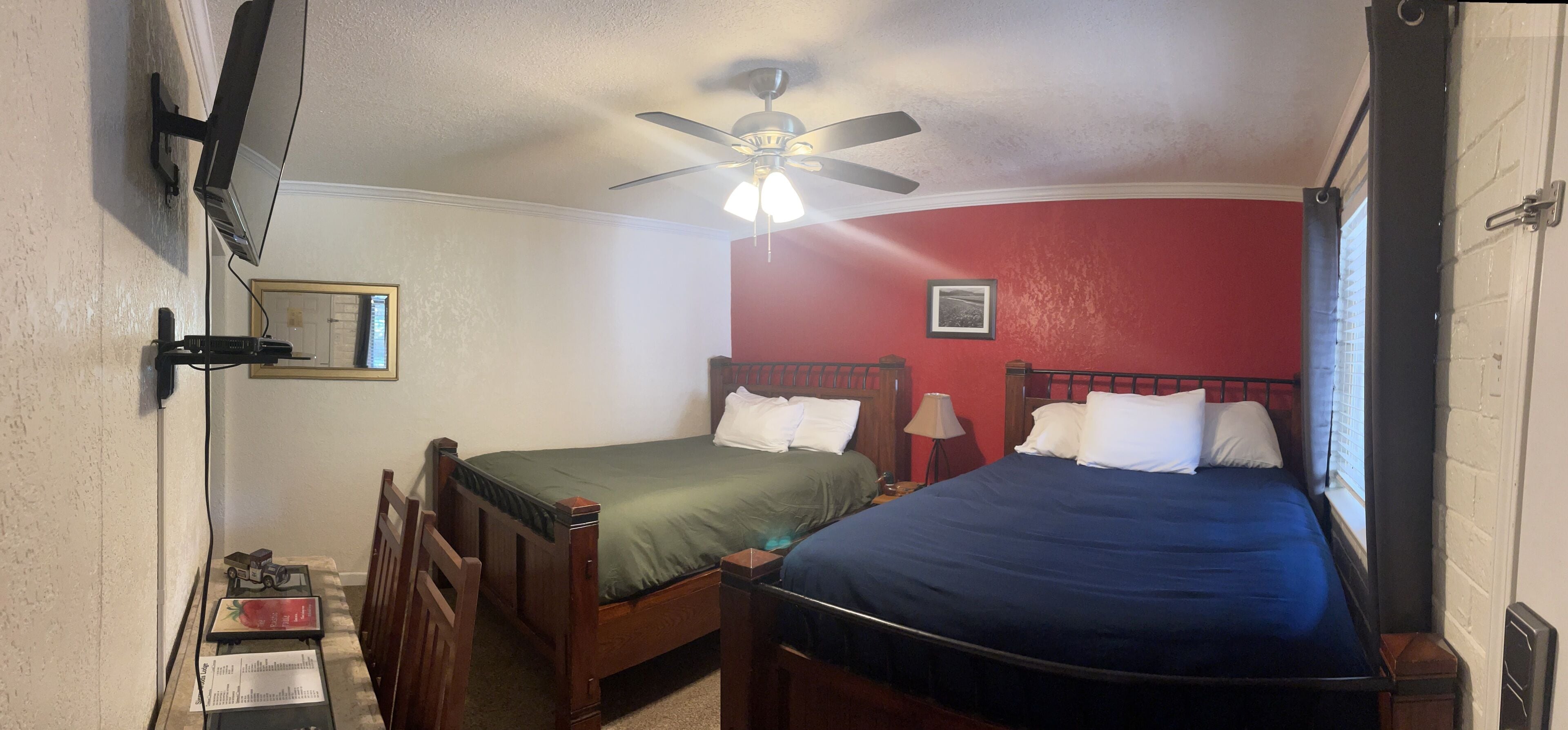 A room with two wooden beds, a ceiling fan, a television, and a small table with a book and a toy.