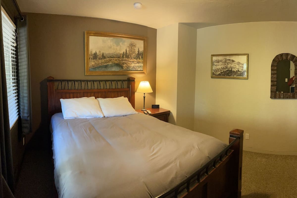 A hotel room with a bed, a desk with a vase of flowers, a television mounted on the wall, and two framed pictures on the wall.