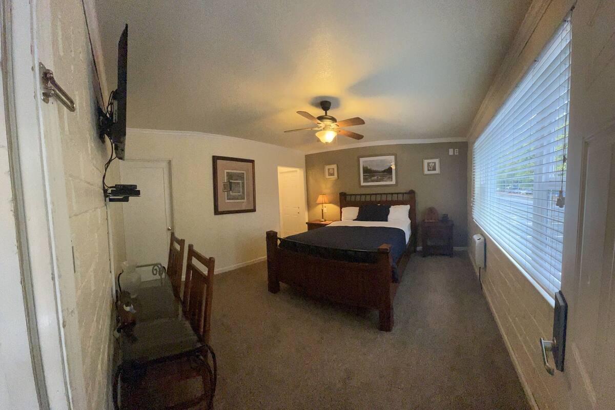 A bedroom with a single bed, a ceiling fan, a nightstand, a chair, and a window with blinds.