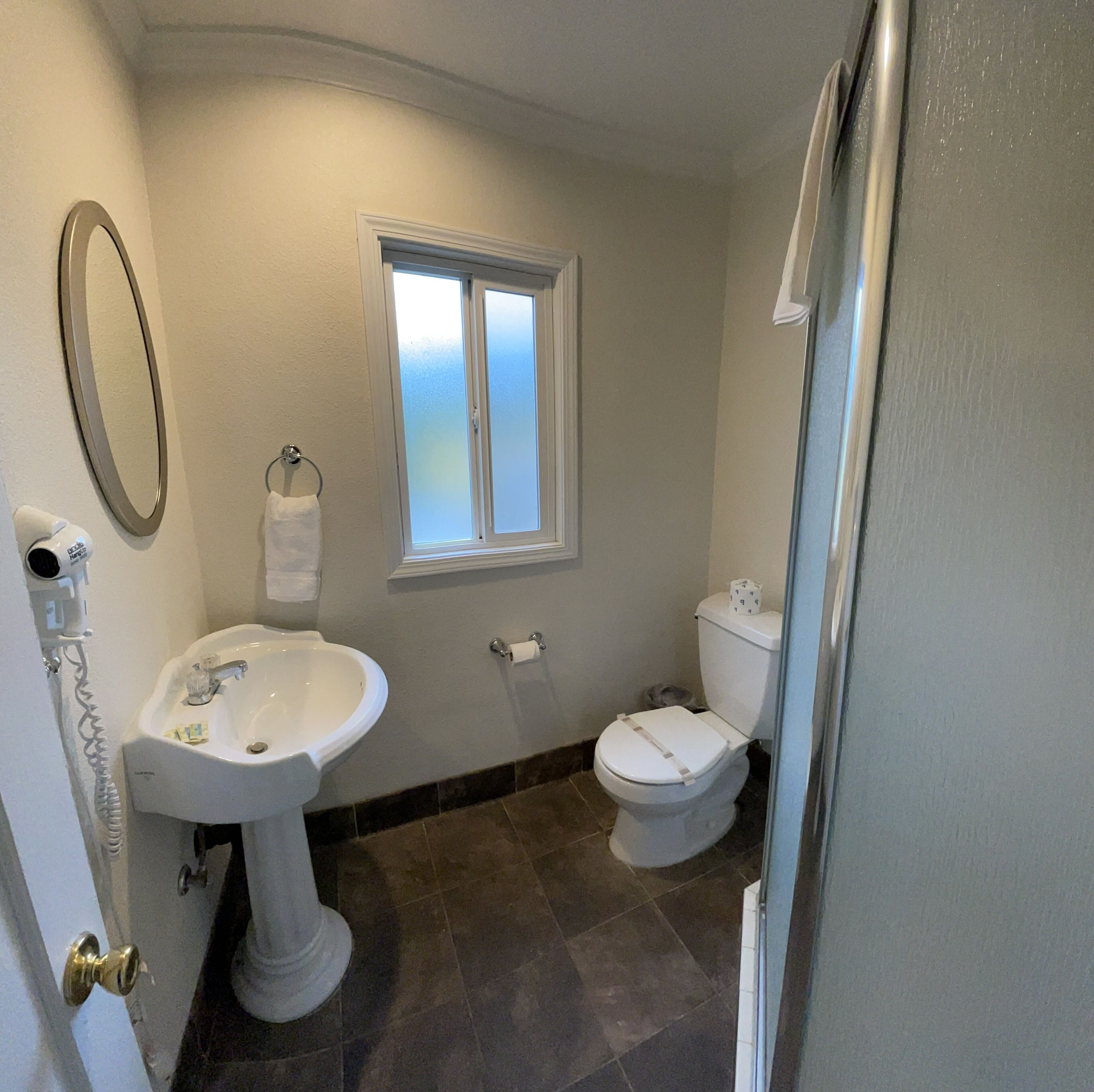 Un baño con lavamanos pedestal, inodoro y ventana.