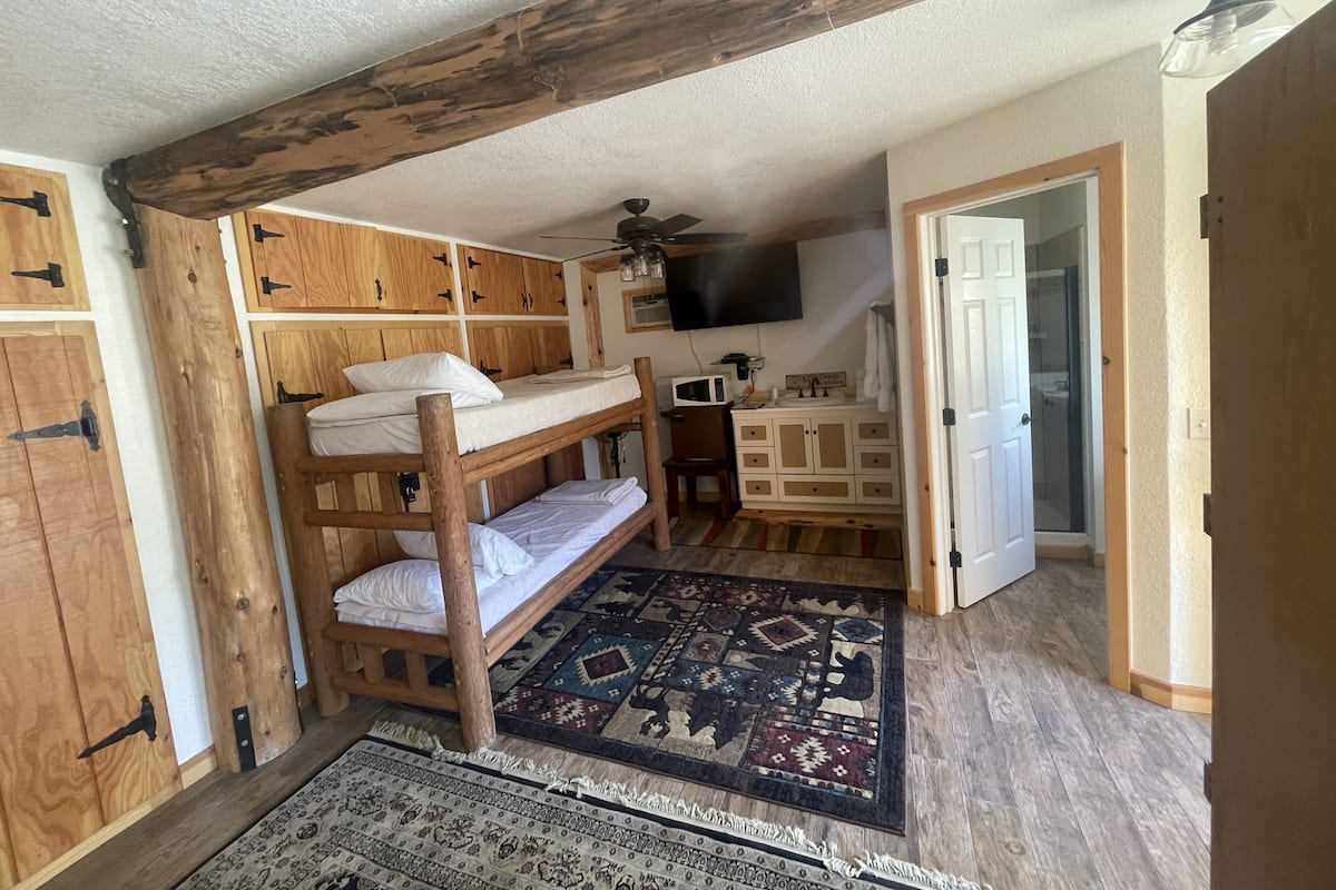 A loft bedroom with a bunk bed, wooden cabinets, a flat-screen TV, and a patterned rug.