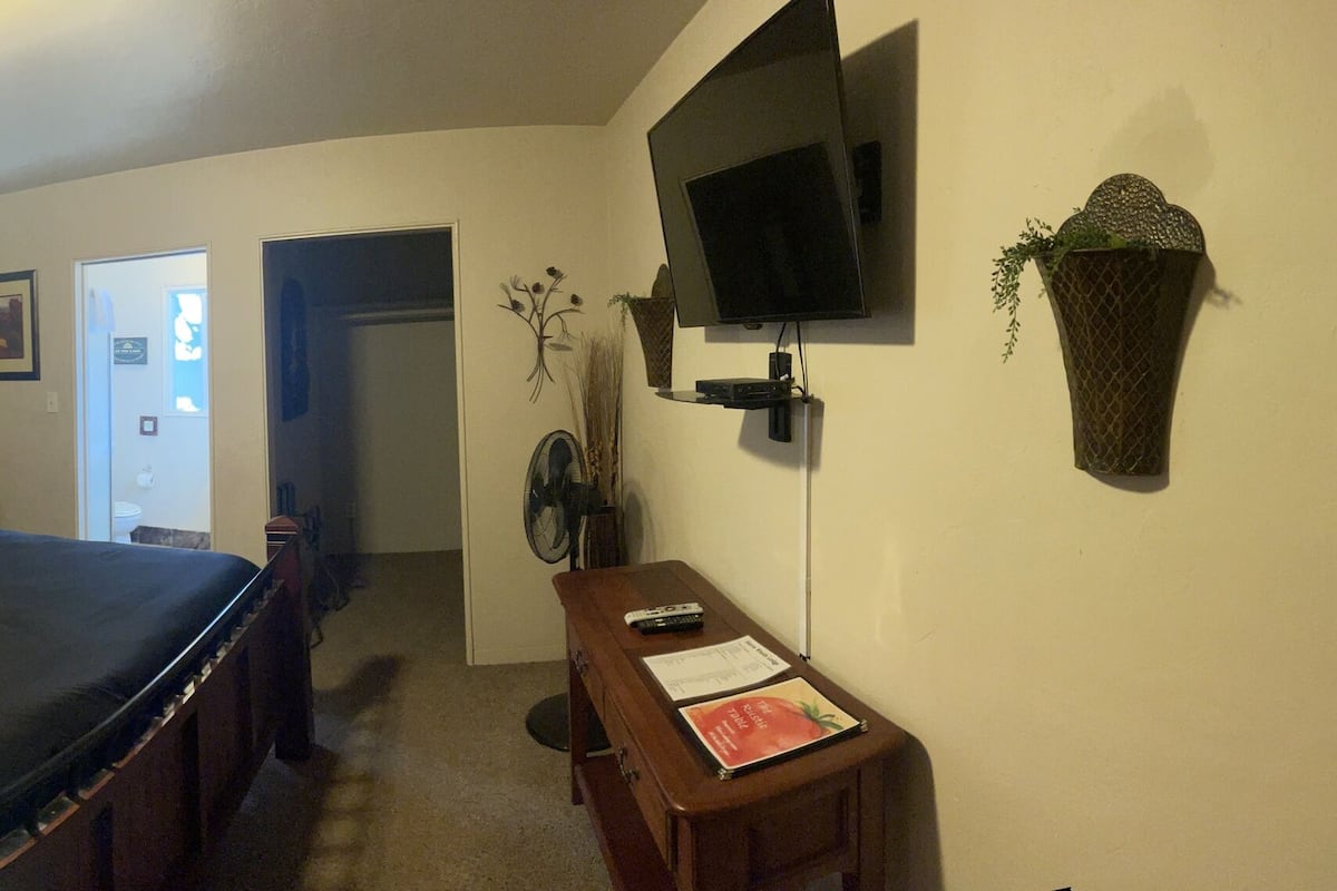A bedroom with a bed, bedside tables, a TV, a mirror, and a door leading to another room.